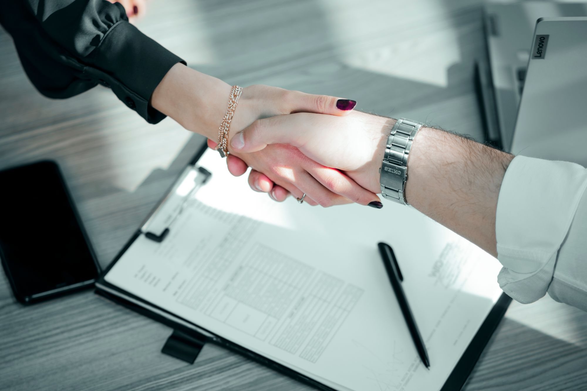 Two people shaking hands over a signed maintenance contract on a clipboard