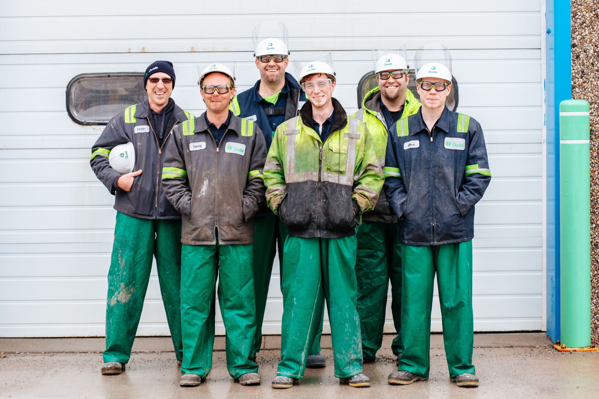 Team of six uniformed maintenance workers in hard hats standing together in front of a service bay