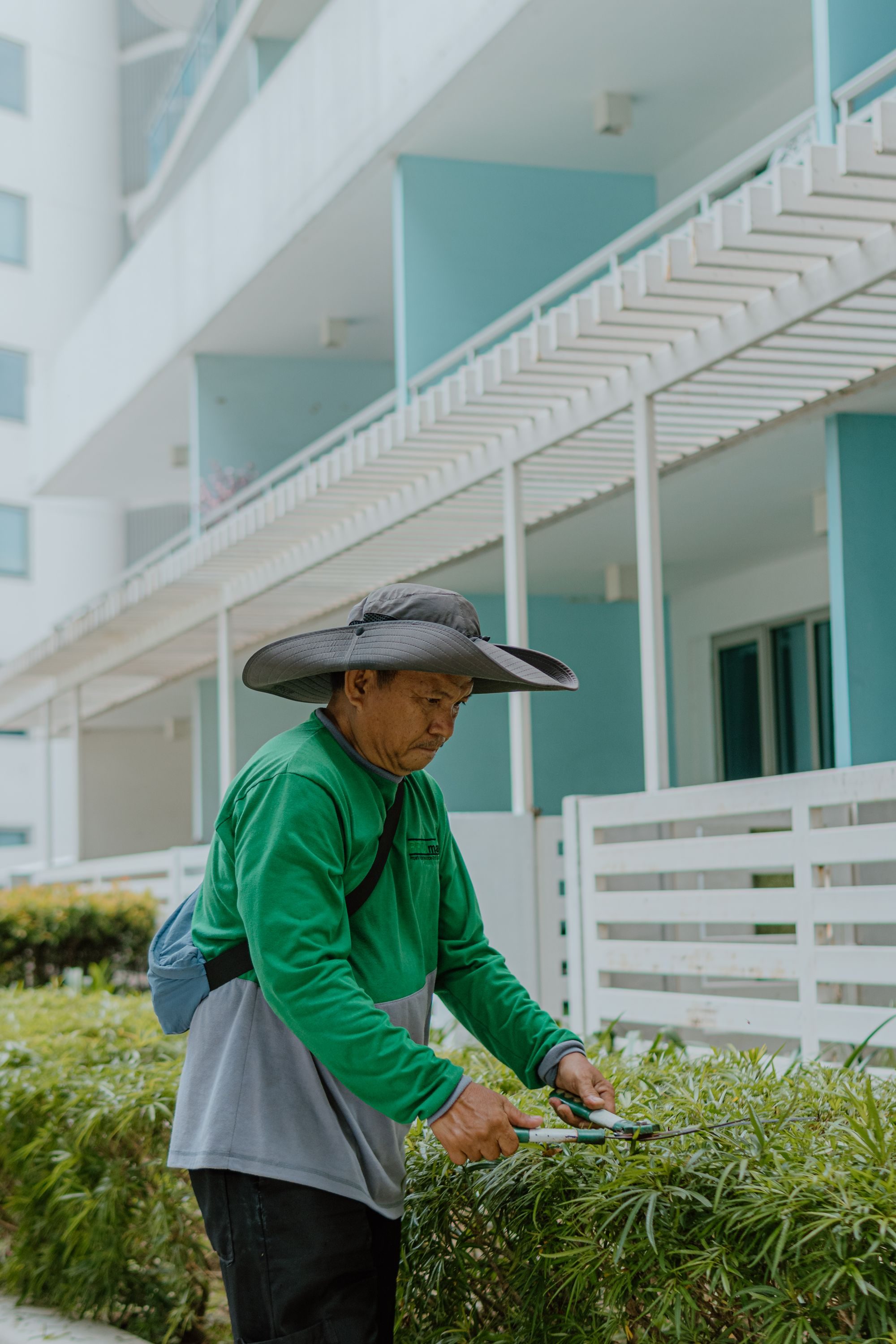 Gardener trimming hedges beside a modern residential building