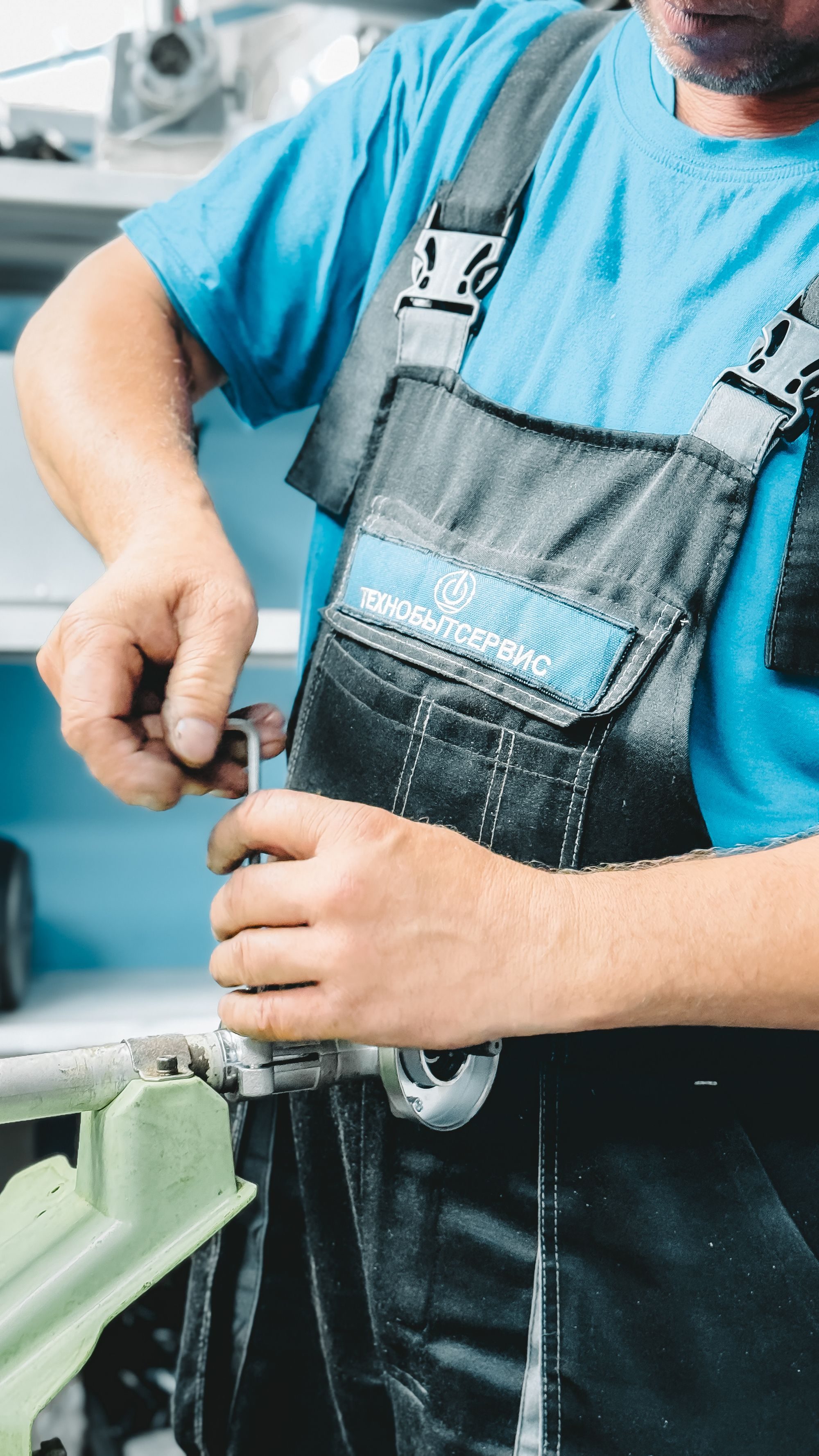 Plumber in blue overalls tightening a pipe fitting with a wrench