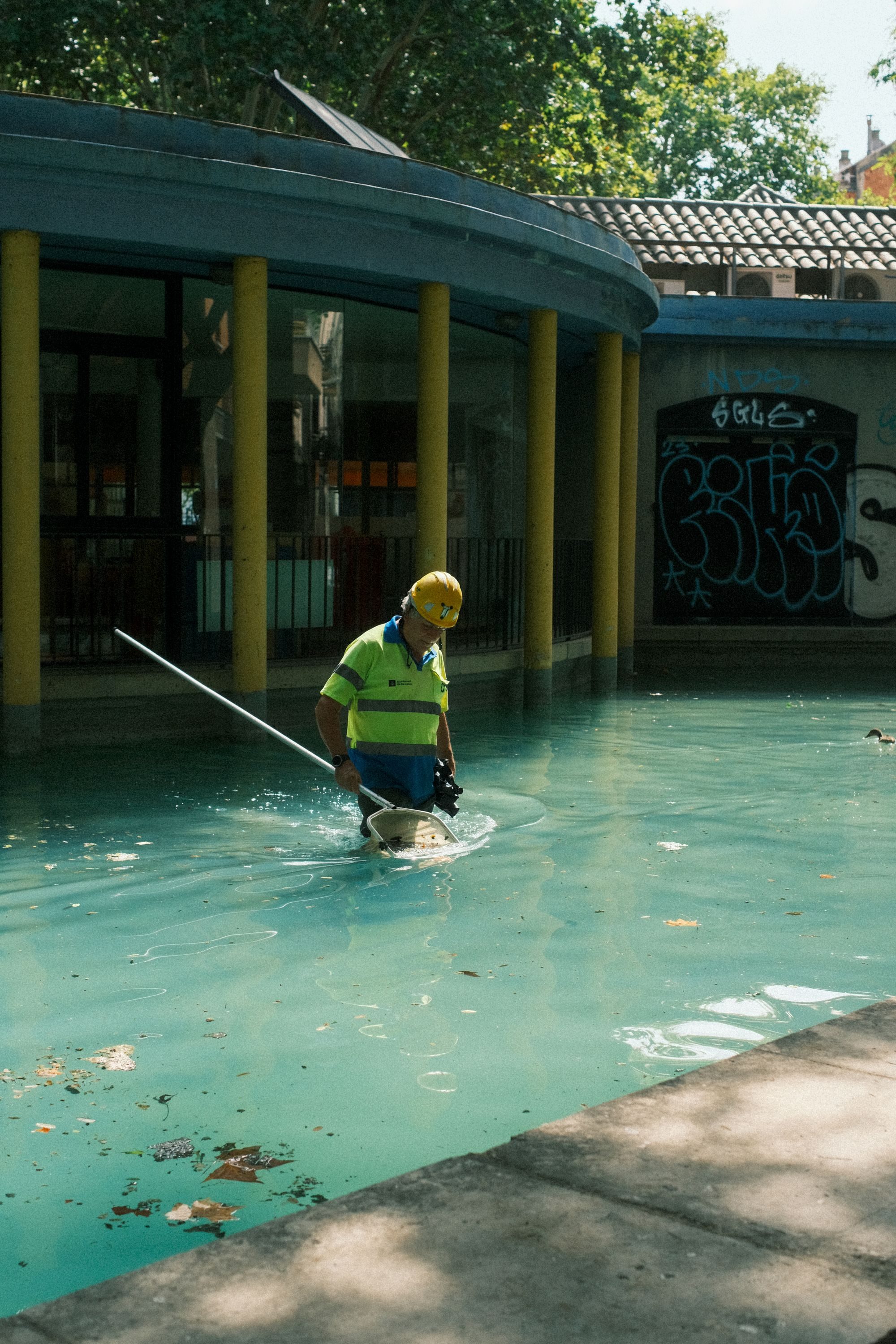 Maintenance worker in high-visibility vest skimming a swimming pool