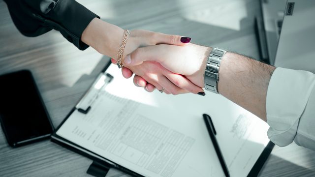 Two people shaking hands over a signed maintenance contract on a clipboard