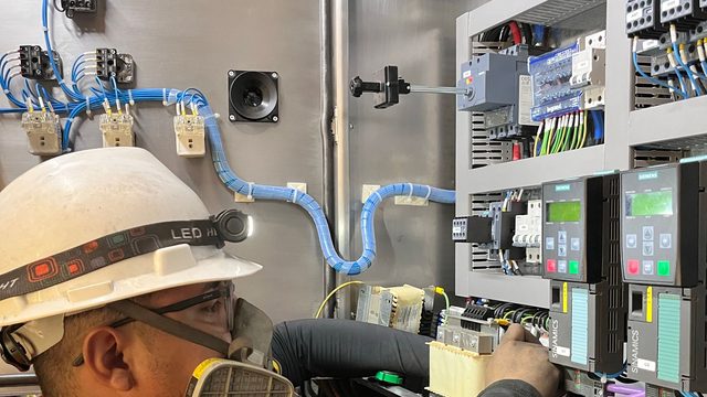 Electrician in safety helmet working on an industrial control panel