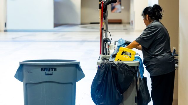 Facility support staff member pushing a cleaning cart along a bright building corridor