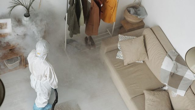 Pest control technician in protective suit misting a room