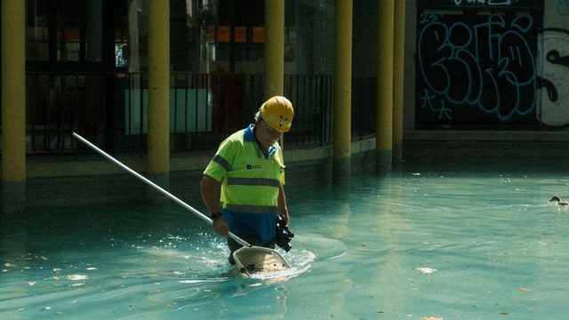 Maintenance worker in high-visibility vest skimming a swimming pool